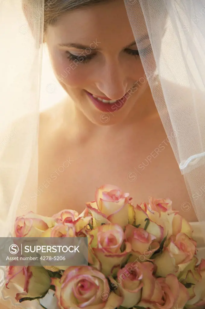 Blushing bride wearing a veil and holding a bouquet of roses