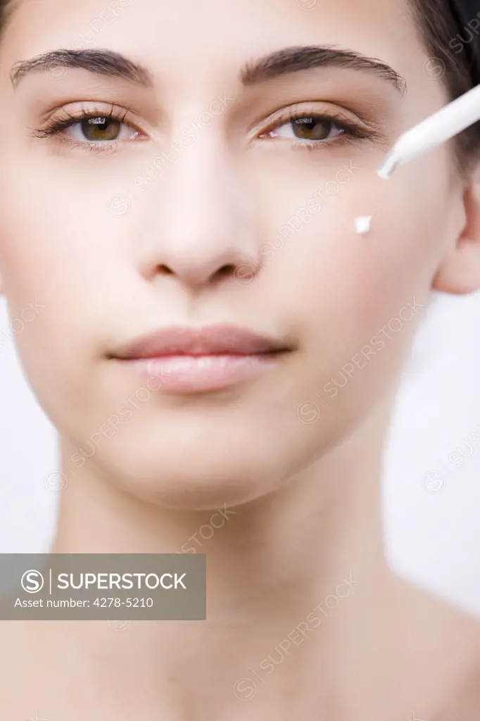 Close up of a young woman applying an anti-aging serum on her face with a dropper