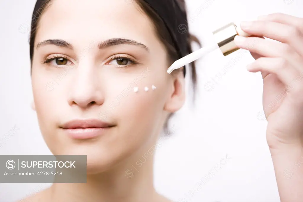 Close up of a young woman applying an anti-aging serum on her face with a dropper