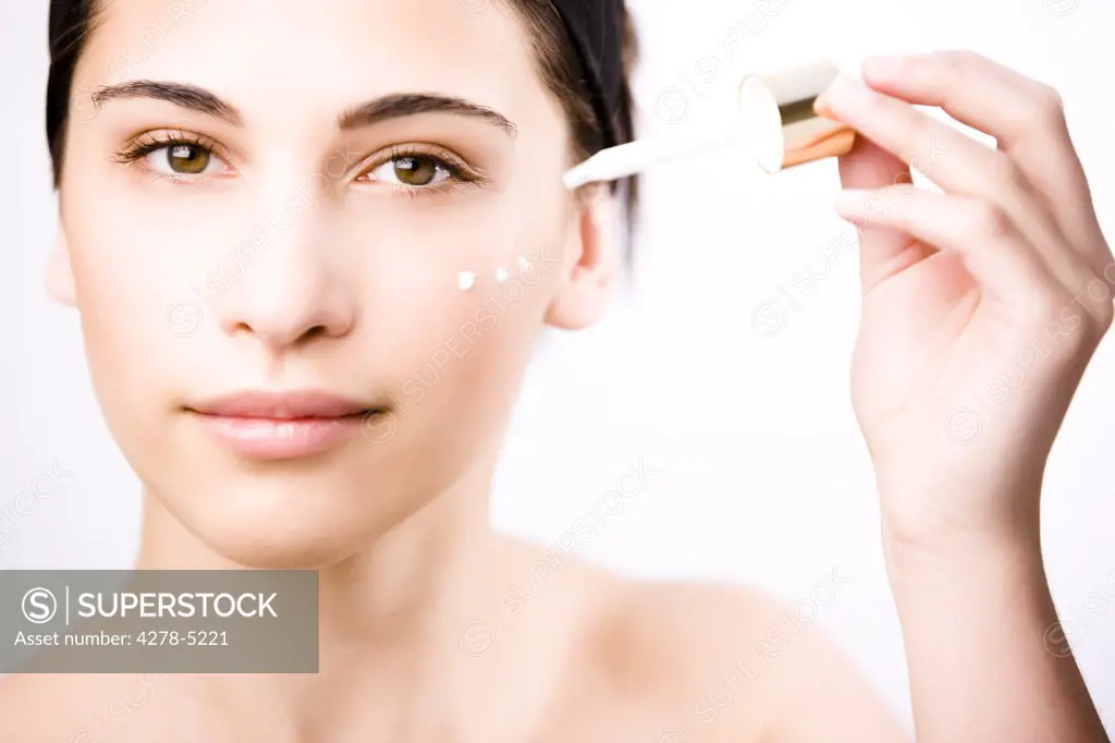 Young woman applying an anti-aging serum on her face with a dropper