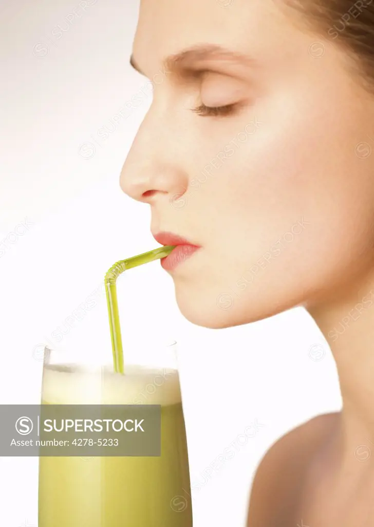 Profile of a woman with eyes closed drinking a vegetable smoothie with a straw