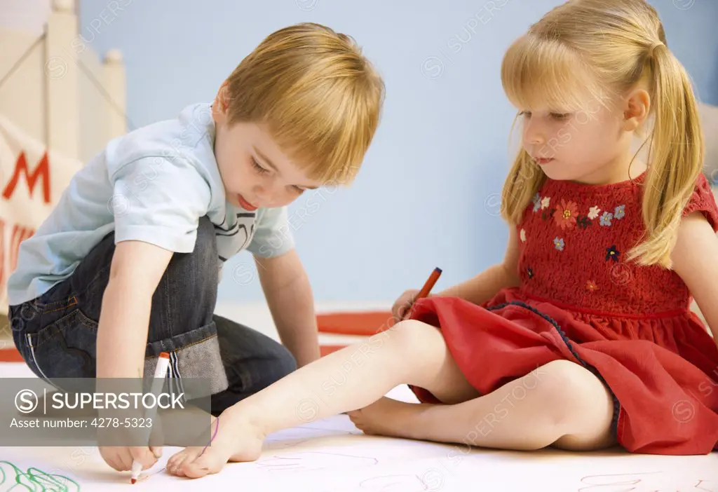 Boy drawing the outline of a girl foot
