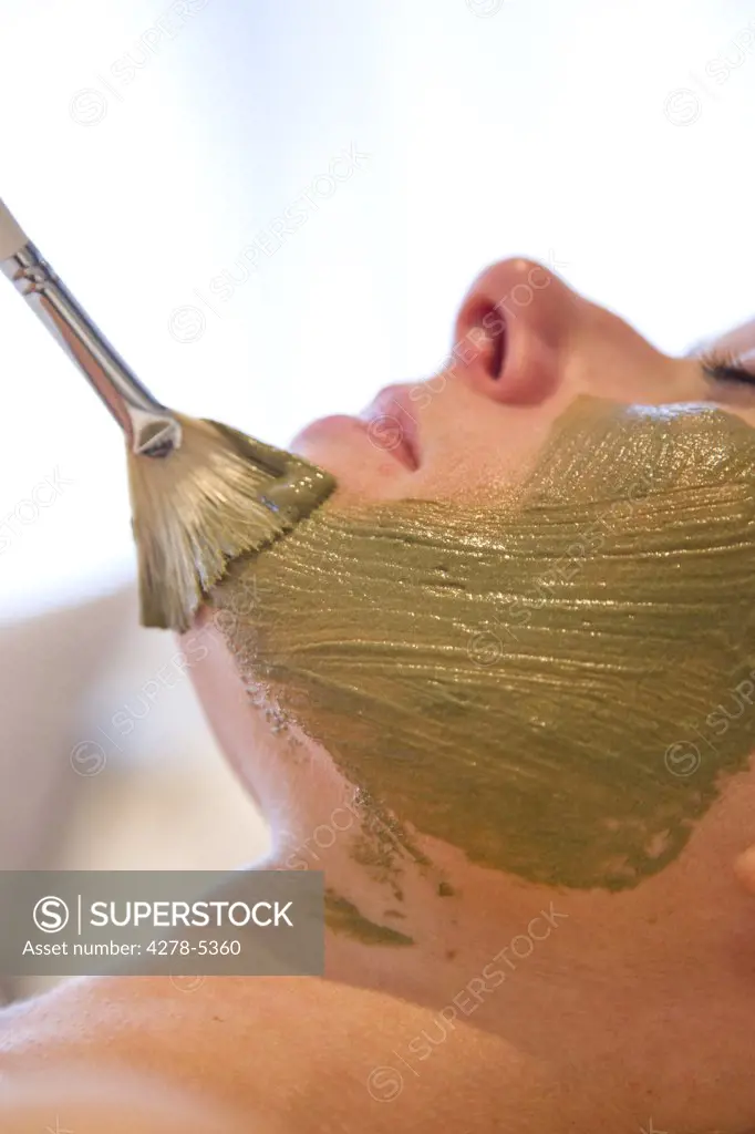 Close up of a brush on a woman face with green beauty mask