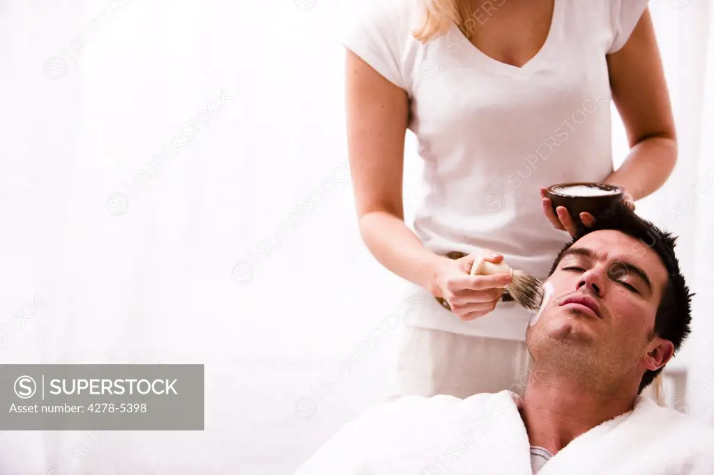 Woman applying shaving cream on man face