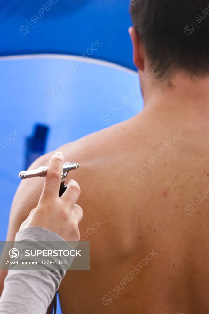 Back view of a man getting a fake tan with an airbrush gun