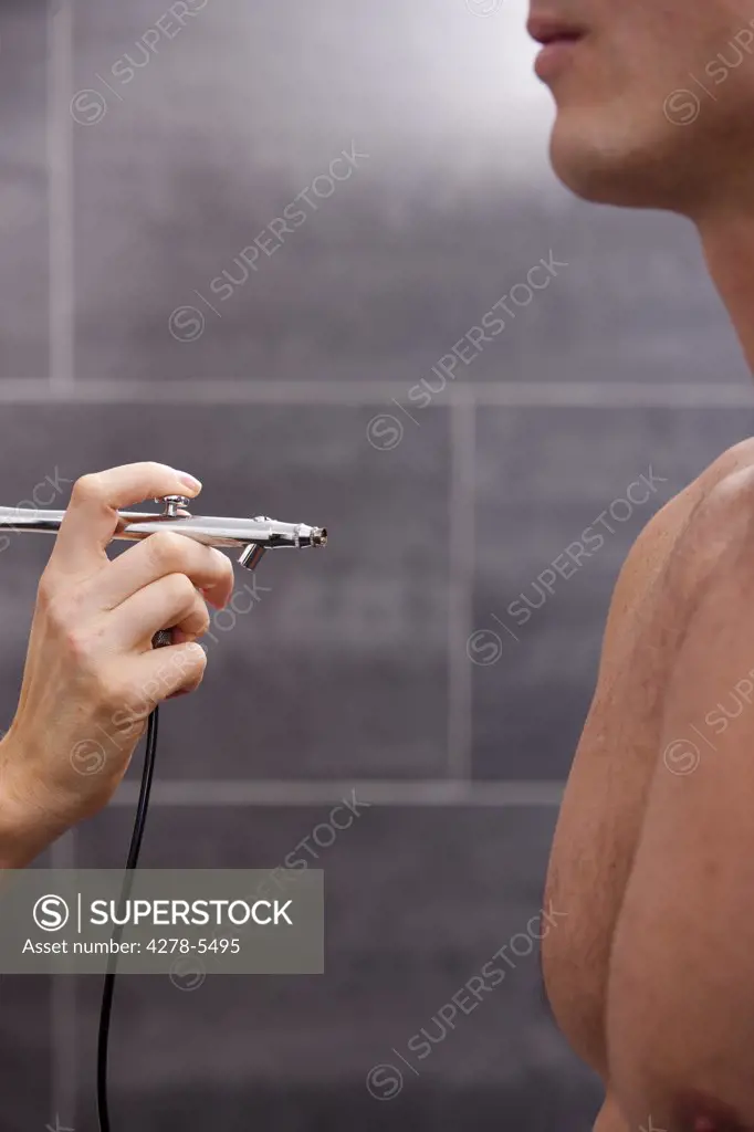 Profile a man getting a fake tan with an airbrush gun