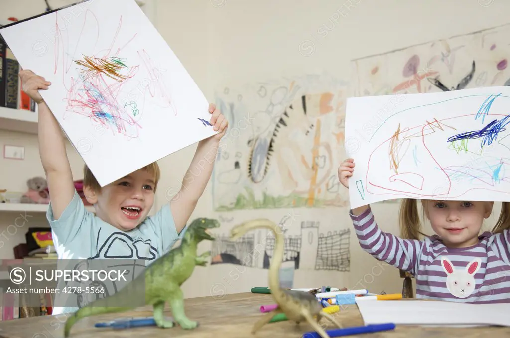 Close up of a boy and girl holding drawings above their heads