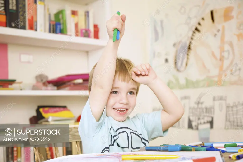 Smiling boy holding coloring pens above his head
