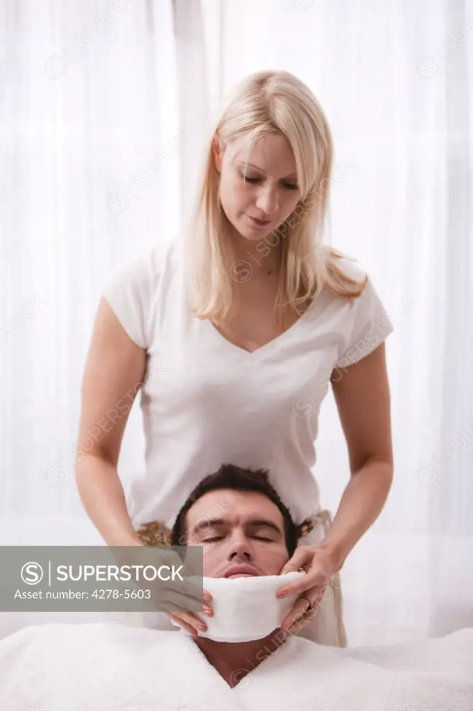 Woman holding hot towel under man chin