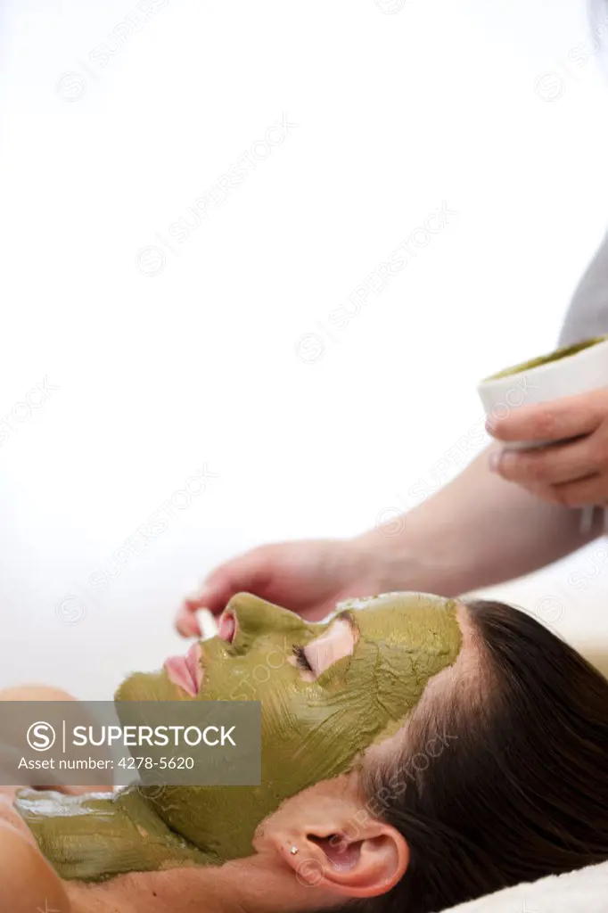 Beautician hand applying green facial mask on woman face