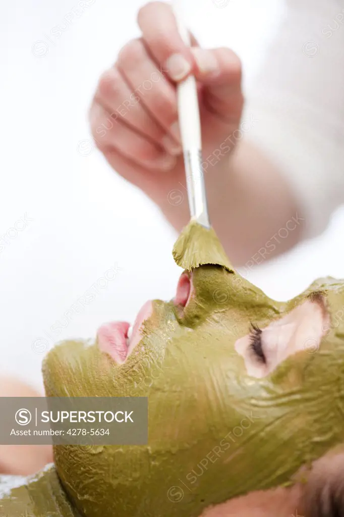 Beautician hand applying green facial mask on woman face with brush