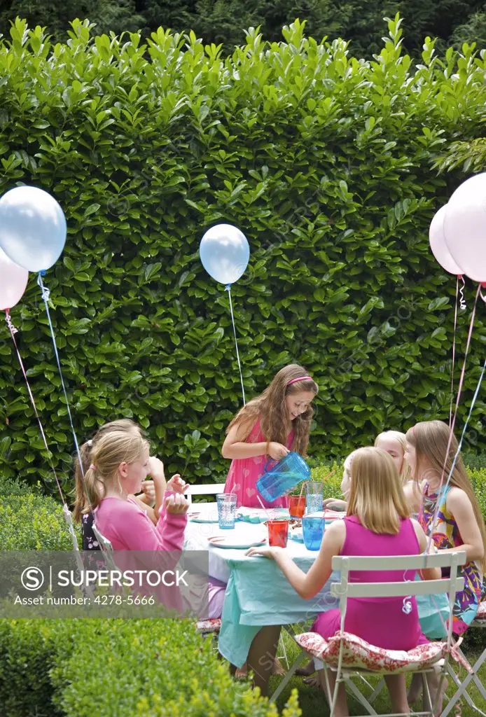 Group of young girls having a party in a garden smiling and laughing