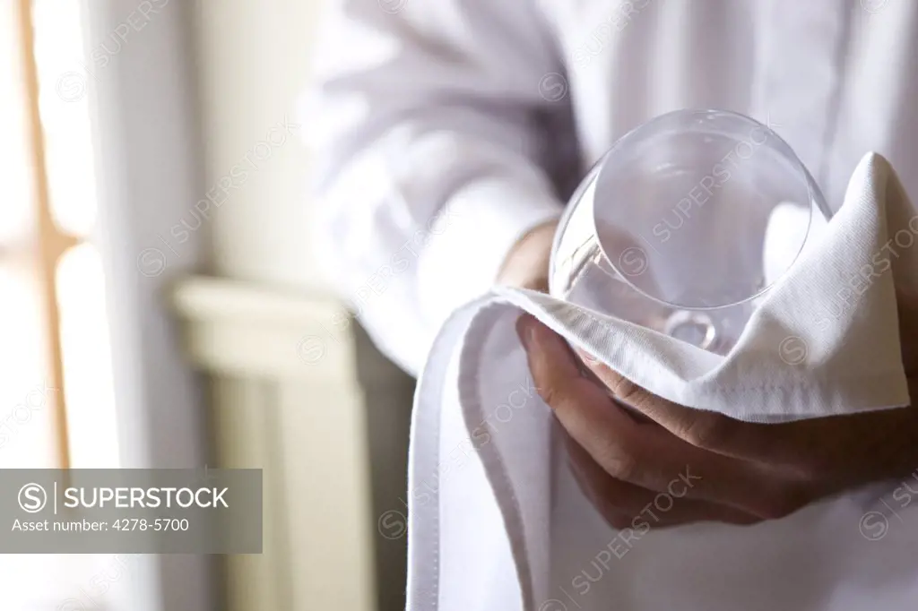 Close up of a waiter's hands polishing a wine glass with a napkin