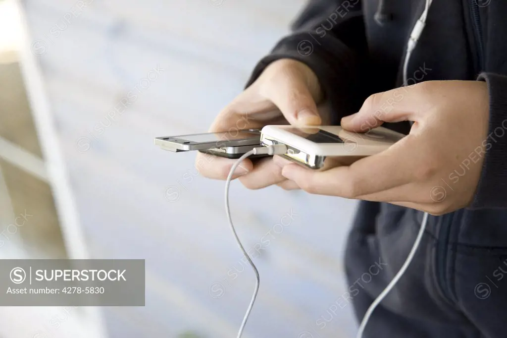 Close up of a boy's hands holding a cell phone and a portable audio player