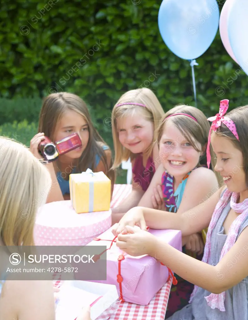 Smiling young girl sitting with friends opening a birthday gift