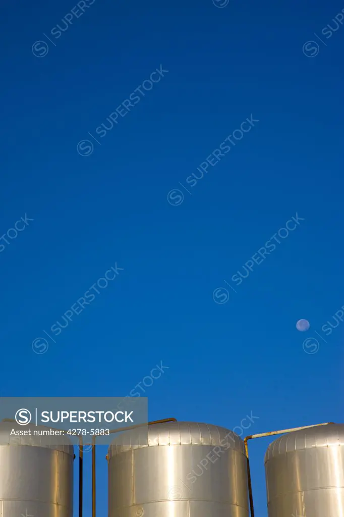 Metal storage tanks against a cloudless blue sky with moon