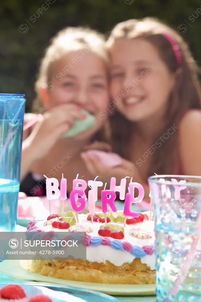 Two smiling young girl sitting behind a birthday cake