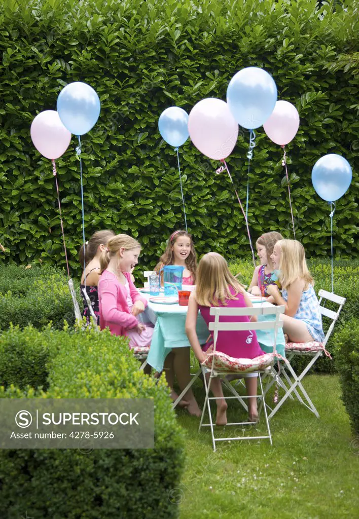 Group of young girls having a party in a garden smiling and laughing