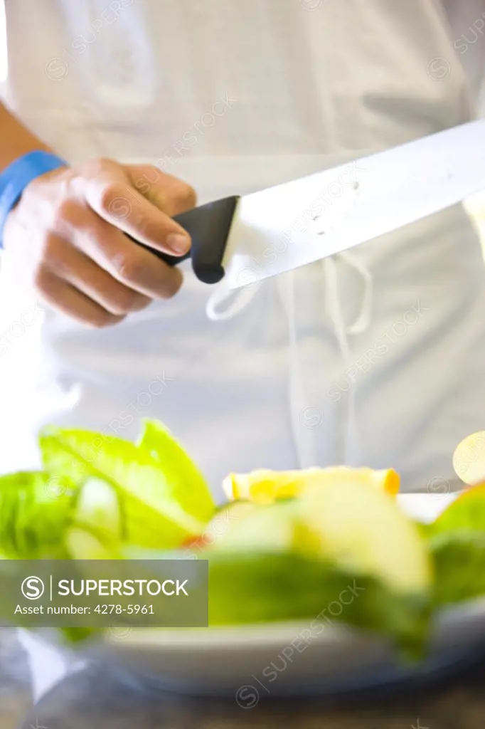 Chef's hand holding a knife standing behind a plate of salad