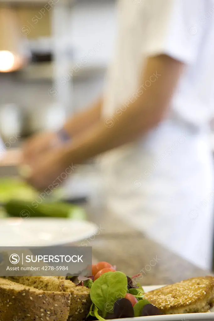 Close up of a mixed salad and bread with a chef standing in the background