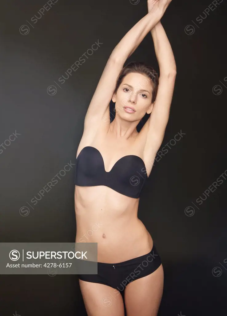 Young woman with arms crossed over head wearing black underwear