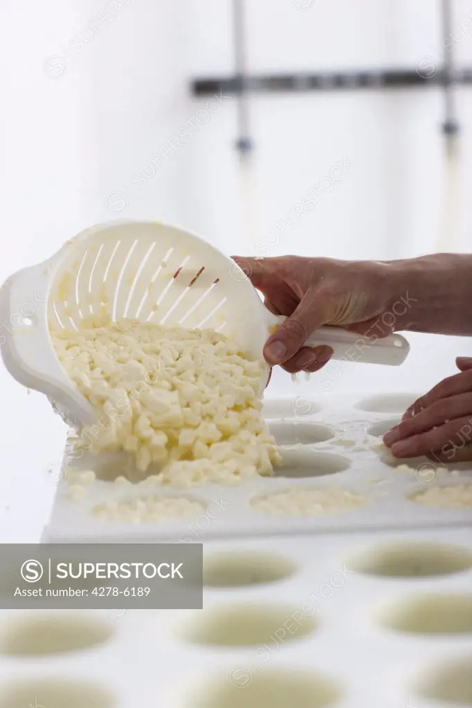 Close up of a man smoothing cheese into moulds