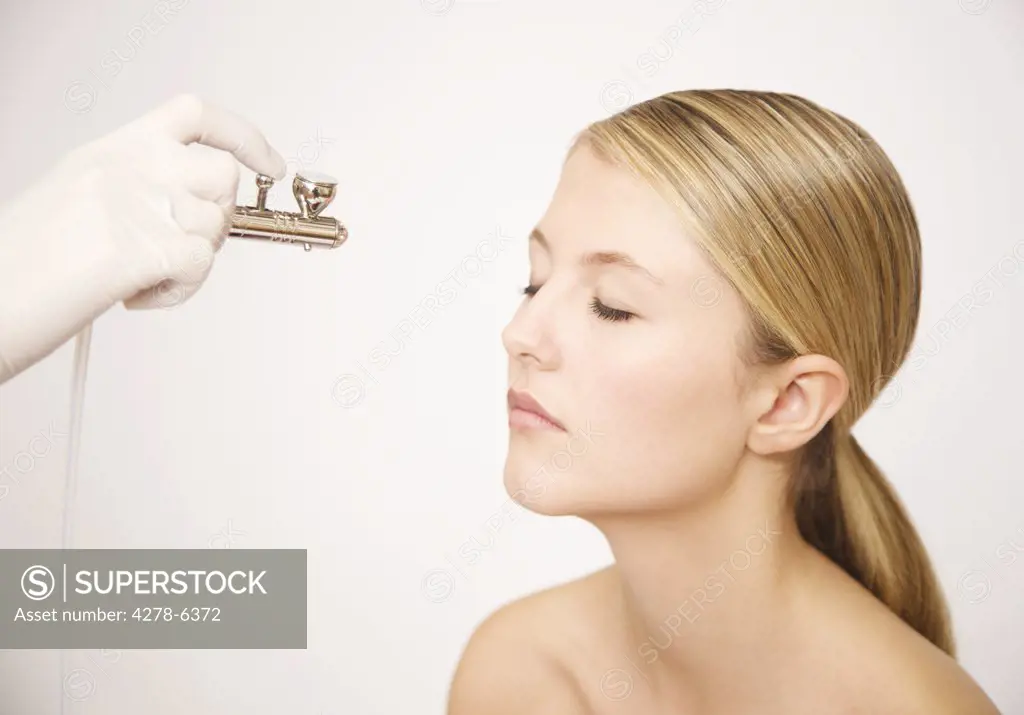 Beautician's hand applying make up with an airbrush to a woman's face