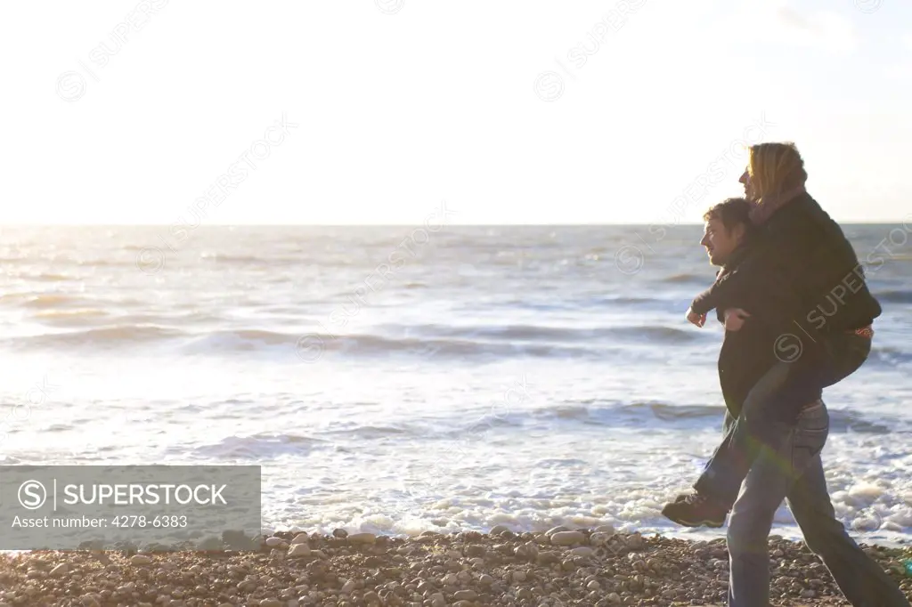 Woman riding piggyback on man on the beach