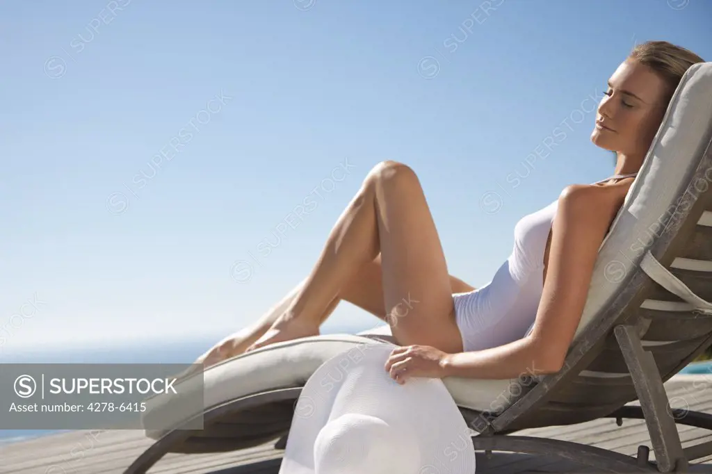 Woman sunbathing on a sun lounger against blue sky