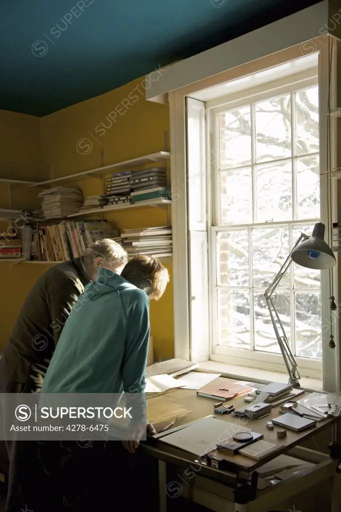 Back view of two men leaning over a desk