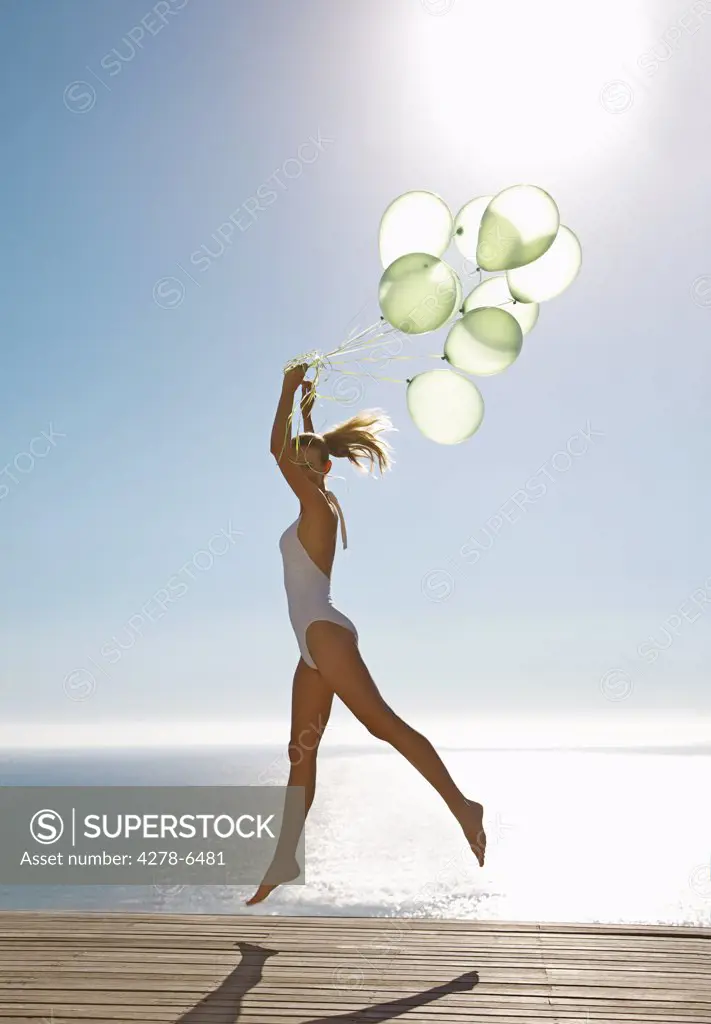 Profile of a woman jumping mid air holding a bundle of green balloons