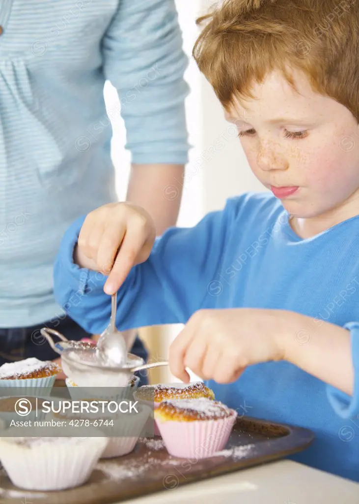 Young boy sprinkling cupcakes with icing sugar