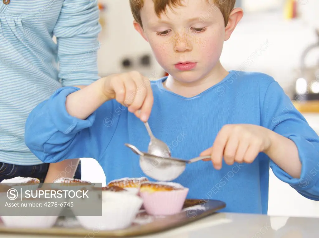 Young boy sprinkling cupcakes with icing sugar