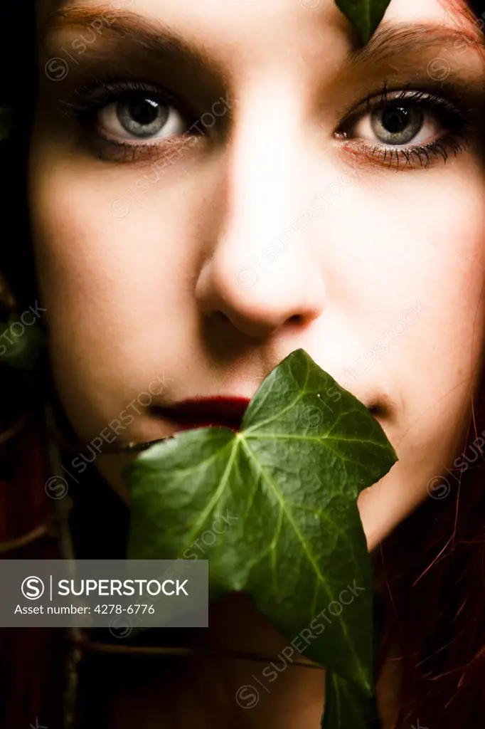 Close up of a woman's face with ivy leaf covering her mouth