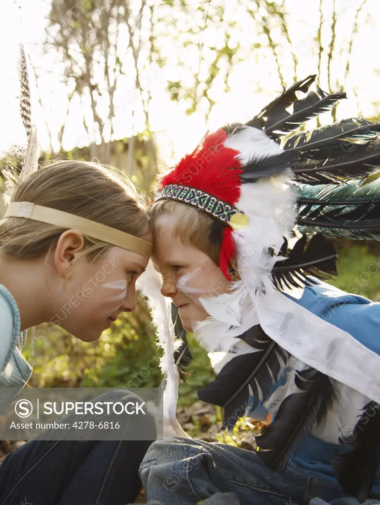 Boy and girl wearing Indian feather headdresses sitting face to face