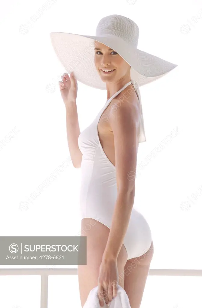 Portrait of a woman in white swimsuit holding the brim of her hat