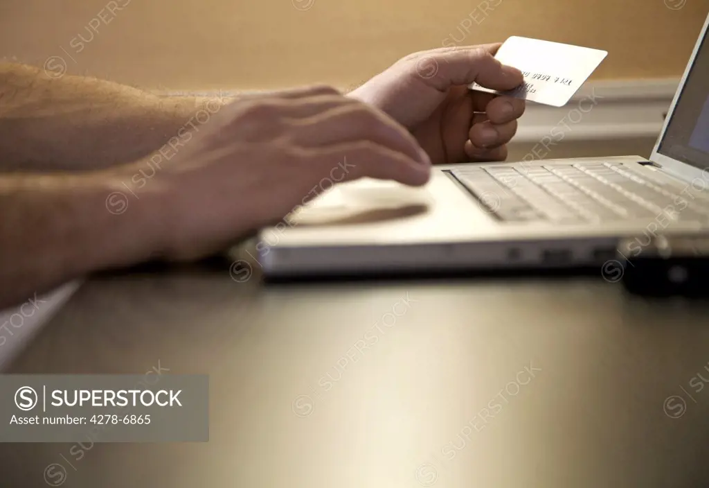 Close up of a man's hands holding a credit card and typing on a keyboard