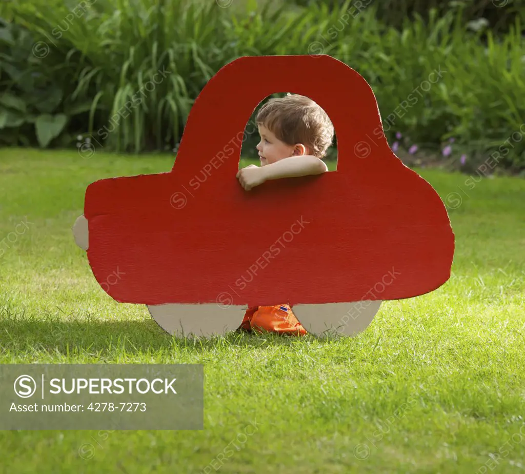Young Boy Kneeling behind Cardboard Cut Out in Shape of Car