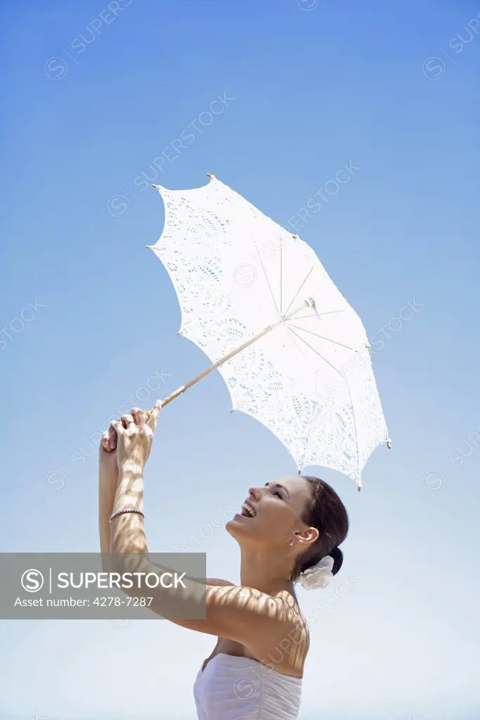 Bride Holding Parasol against Blue Sky