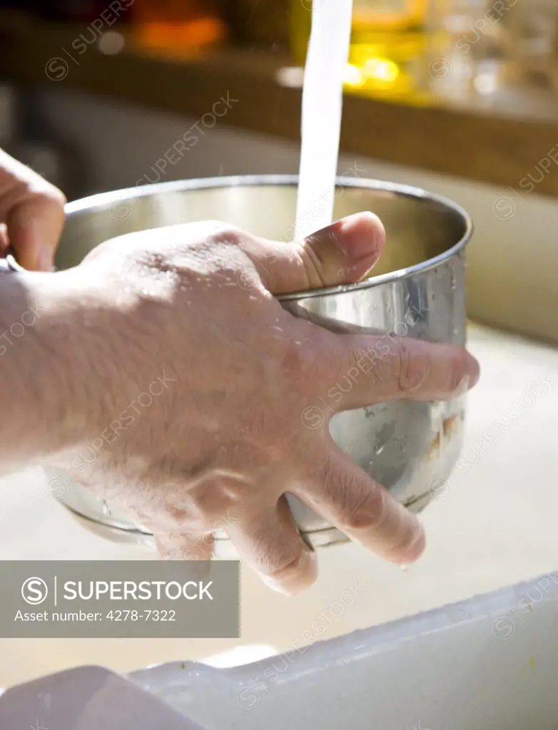 Man's Hand Holding Pan under Running Water over Sink