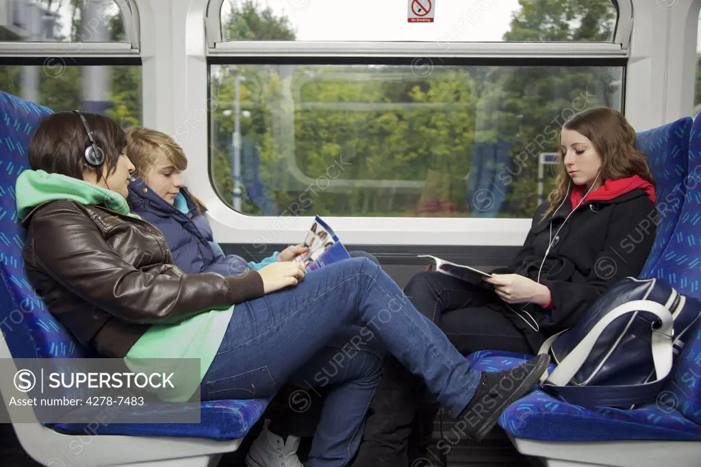 Teenage Girls Sitting on Train Reading and Listening to Music