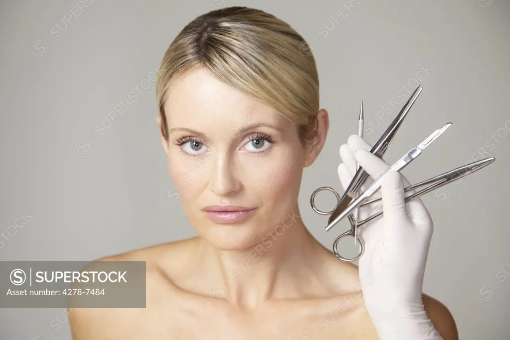 Doctor's Hand Holding Surgical Instruments in front of Woman's Face