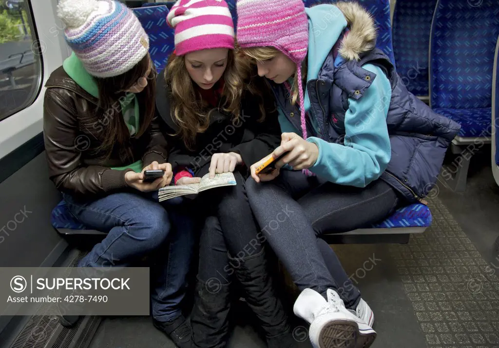 Teenage Girls Sitting on Train Inspecting a Guidebook