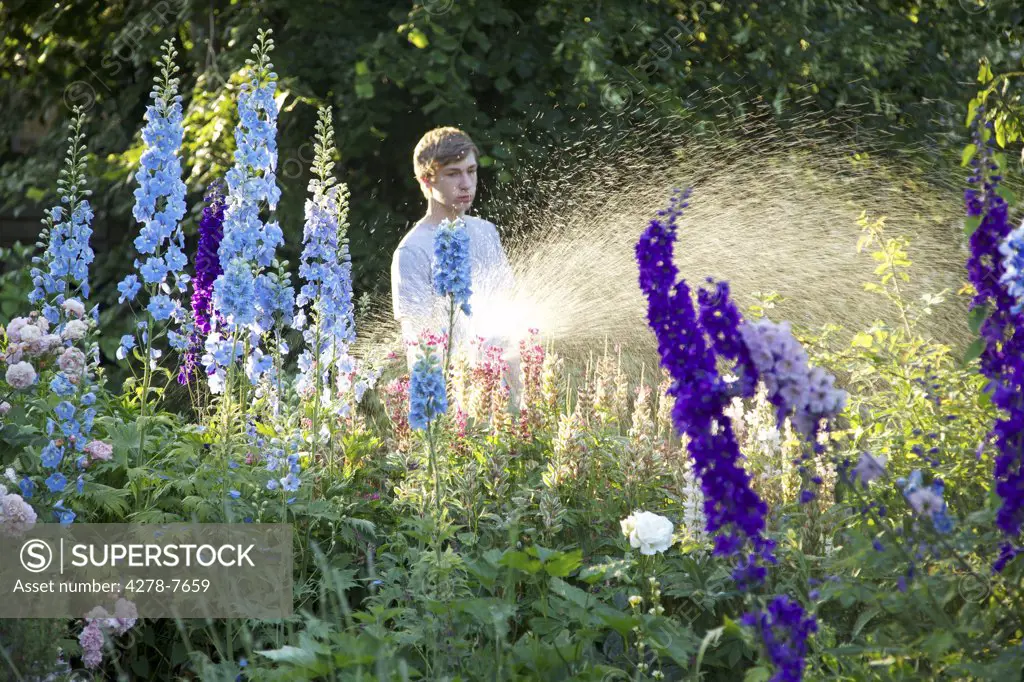 Teenage Boy Watering Flowers with Garden Hose
