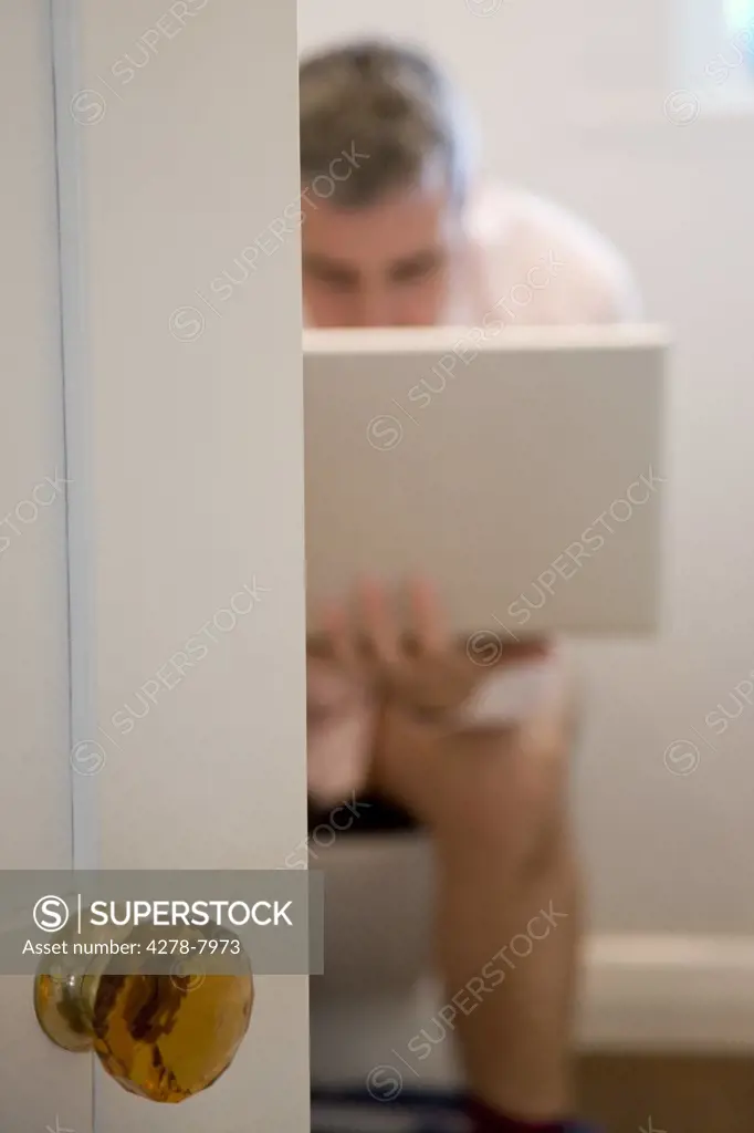Man Sitting on Toilet Using Laptop
