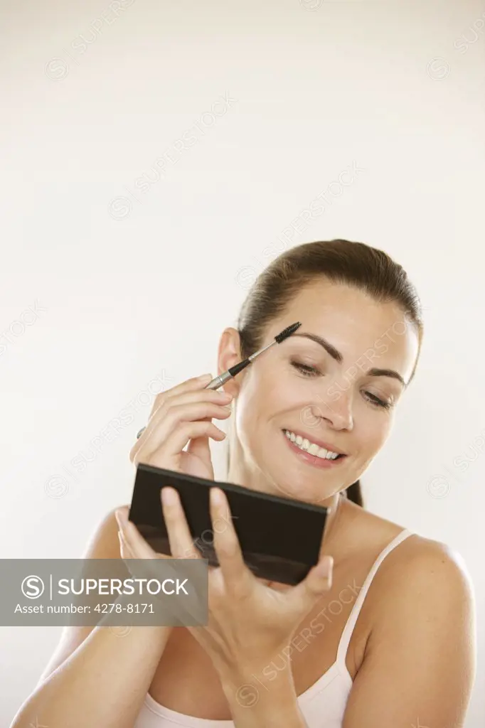 Woman Holding Handheld Mirror Using Eyebrow Brush