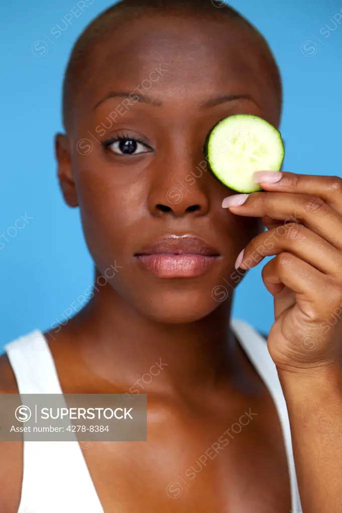 Young Woman Holding Cucumber Slice over Eye
