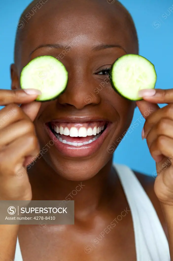Smiling Woman Holding Cucumber Slices over Eyes