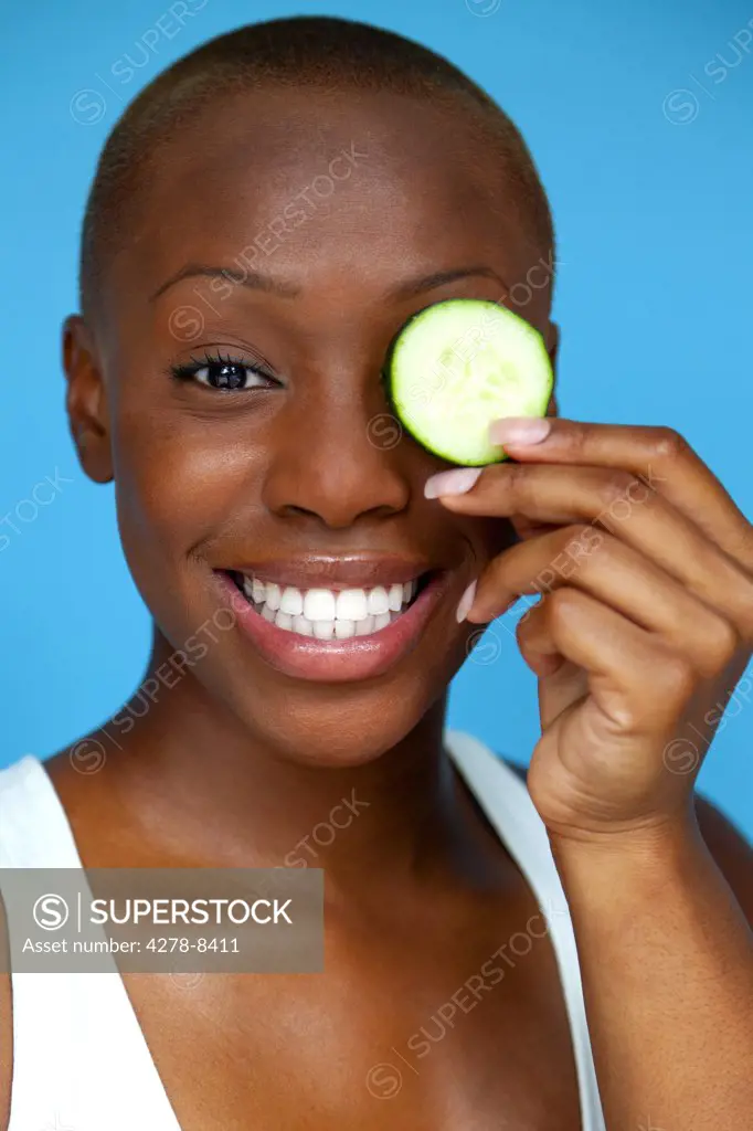 Smiling Woman Holding Cucumber Slice over Eye