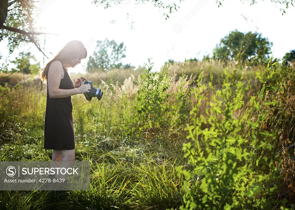 Woman Standing in a Meadow Holding Vintage Camera